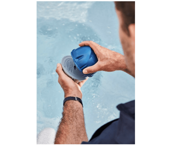 A man is holding a FROG @Ease Floating Sanitizing System for Hot Tubs, Quick and Easy Self-Regulating Hot Tub Sanitizer with Sanitizing Minerals and SmartChlor Technology in the water.